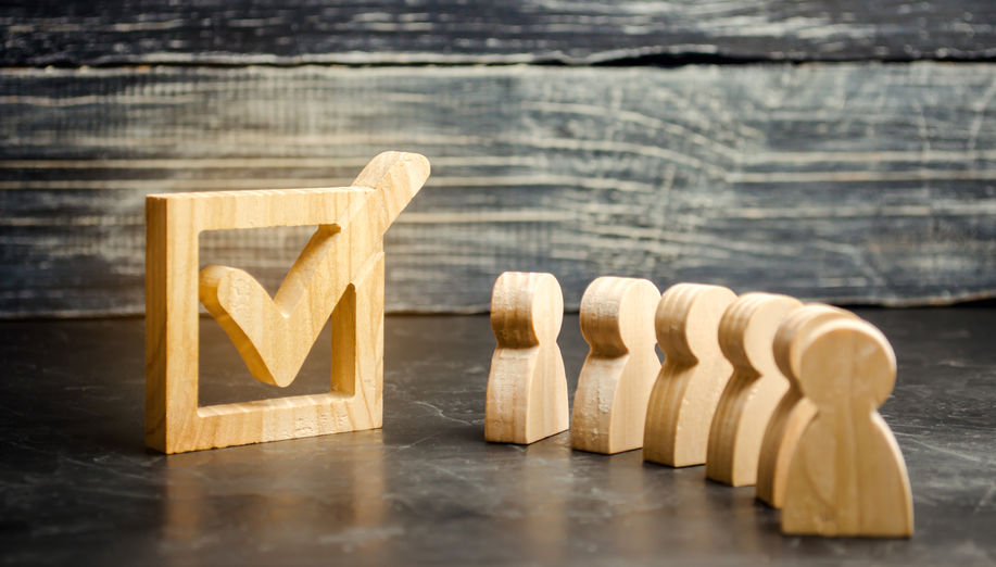 Wooden human figures stand together next to a tick in the box. The concept of elections and social technologies. Volunteers, parties, candidates, constituency electorates. Human rights. referendum
